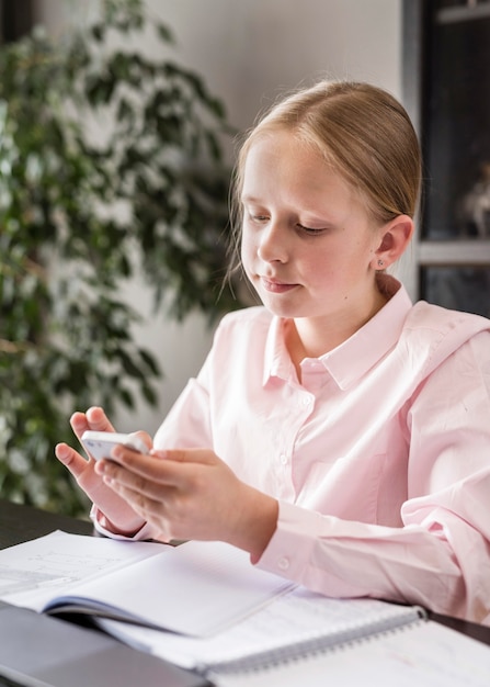 Photo gratuite petite fille vérifiant son téléphone en classe en ligne