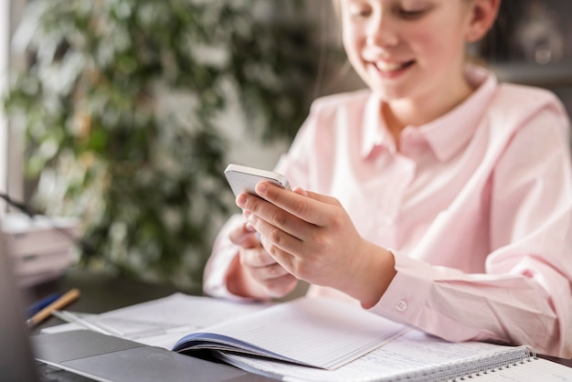 Photo gratuite petite fille vérifiant son téléphone en classe à la maison