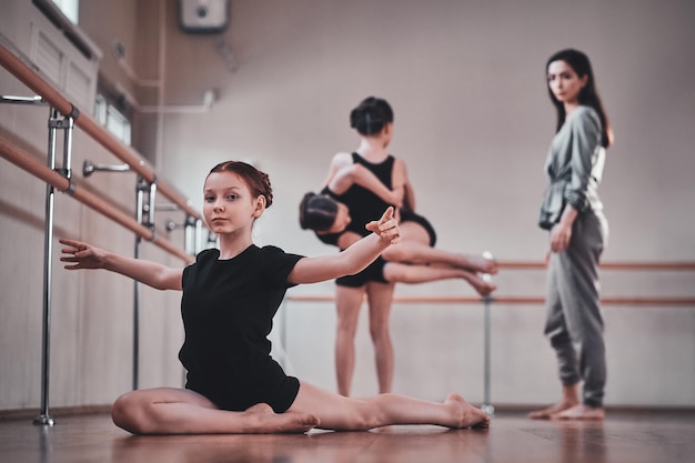 Petite jolie fille fait des étirements pendant que ses autres camarades de classe font des exercices avec le professeur.