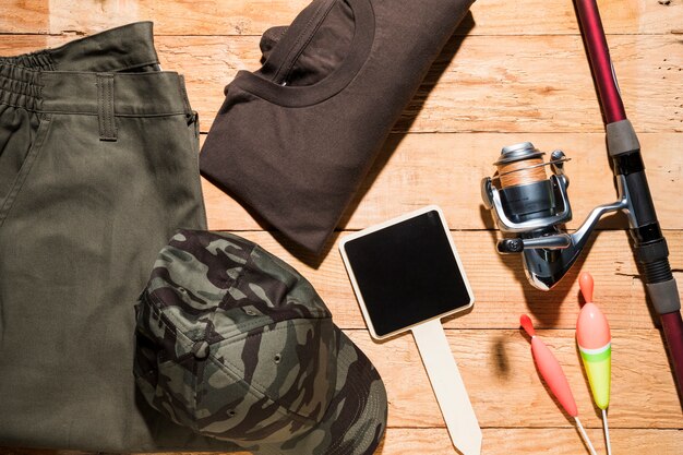 Photo gratuite petite plaque vierge; flotteurs de pêche; canne à pêche et vêtements masculins sur un bureau en bois