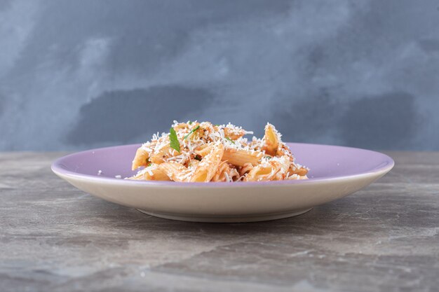 Une petite portion de pâtes penne, sur la surface en marbre.