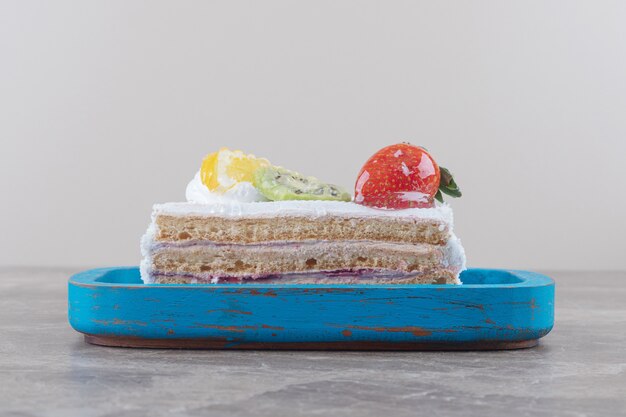 Petite tranche de gâteau avec garniture de fruits sur un plateau sur marbre