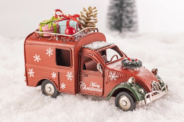 Petite voiture jouet décorée d'ornements sur la neige artificielle avec un arbre de Noël en arrière-plan