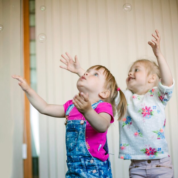 Des petites filles attrapent des bulles de savon dans la pièce