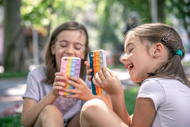 Petites filles à l'extérieur avec des téléphones dans un étui à boutons, un jouet anti-stress tendance.