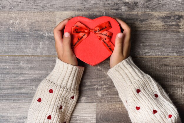 Les petites mains de jeune fille tenant une boîte cadeau en forme de coeur