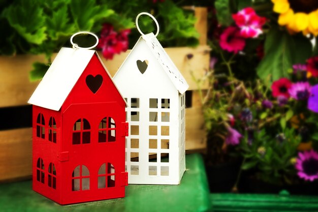 Petites maisons de jardin mignonnes avec des fenêtres en forme de coeur sur la table en bois vert dans le jardin avec de belles fleurs sur fond.