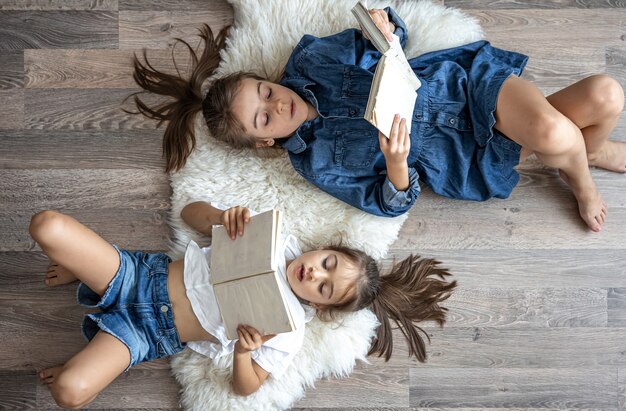 Les petites sœurs des filles lisent des livres allongés sur le sol, vue de dessus.