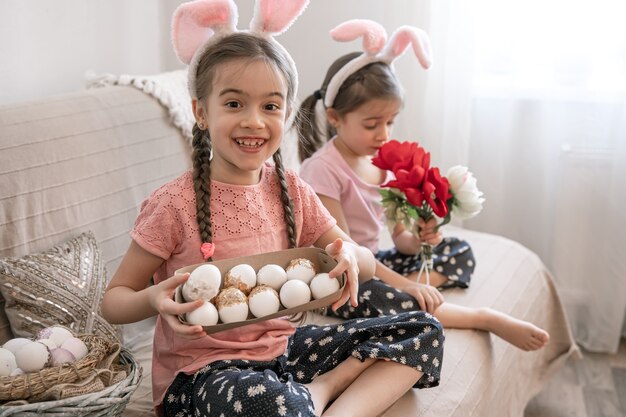 Petites soeurs avec des oreilles de lapin posent avec des oeufs de Pâques et des fleurs pour la décoration