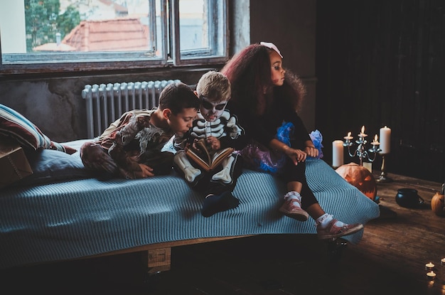 Les petits amis attendent la fête d'Halloween en lisant un livre et assis sur le lit.