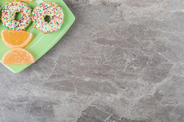 Petits beignets et confitures disposés sur un plateau vert sur une surface en marbre