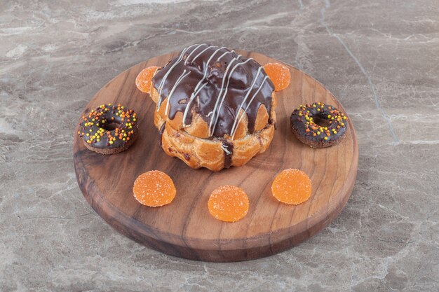 Petits beignets, confitures et gâteau enrobé de chocolat sur une planche en bois sur une surface en marbre