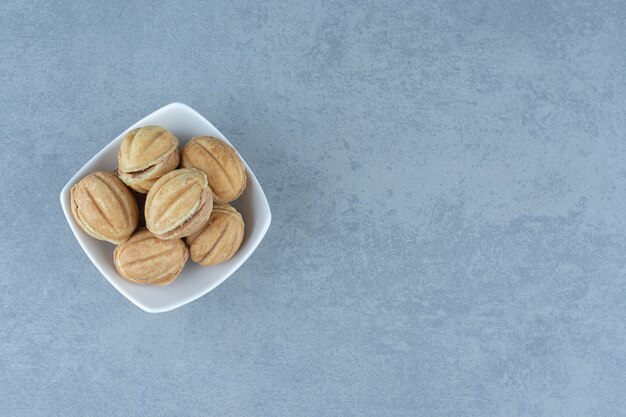 Petits biscuits faits maison sous forme de noix dans un bol blanc sur gris.