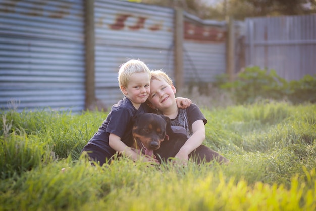 Petits garçons mignons assis joyeusement sur l'herbe et posant avec un chien rottweiler