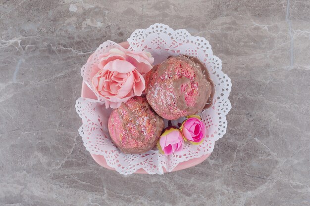Petits gâteaux et corolles de fleurs dans un bol recouvert de napperon sur marbre