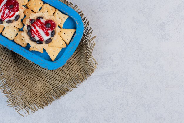 Petits gâteaux et craquelins dans un plateau bleu sur table en marbre.