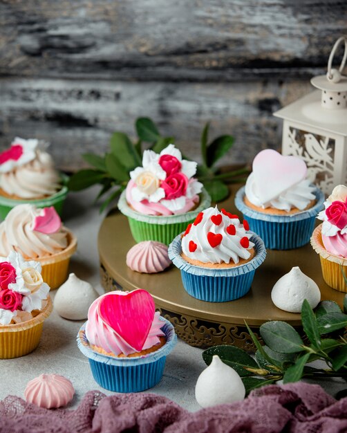 Petits gâteaux mignons décorés de coeurs de crème fouettée et de fleurs