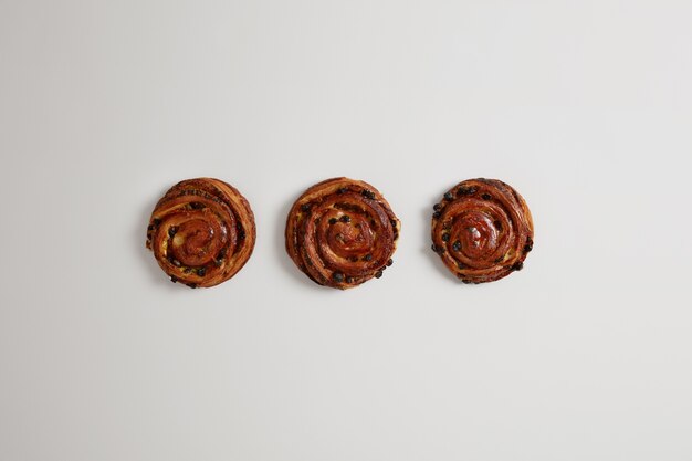 Petits pains appétissants sucrés aux raisins secs isolés sur fond blanc. Dessert frais cuit au four pour les gourmands de la boulangerie. Produits de confiserie. Concept d'aliments riches en calories. Cannelle danoise