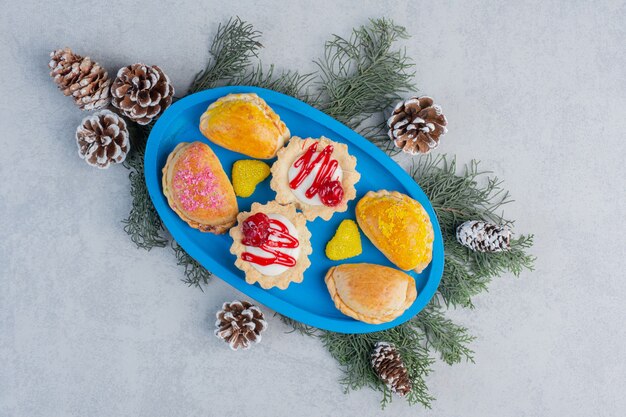 Petits Pains, Cupcakes Et Bonbons à La Gelée Sur Un Plateau Bleu Décoré De Feuilles De Pin Et De Cônes Sur Une Surface En Marbre