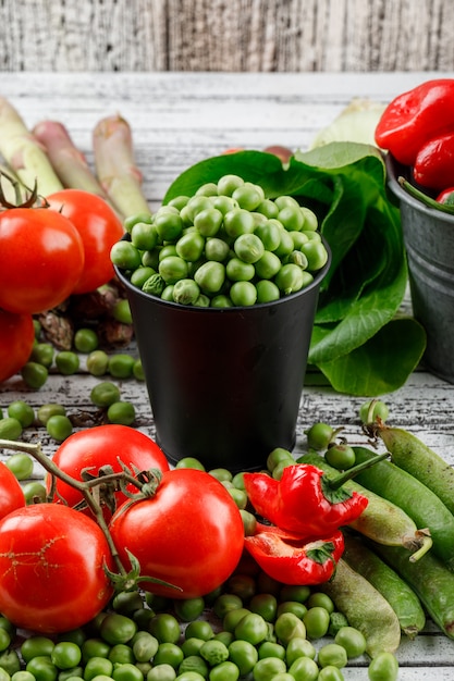 Petits pois dans un mini seau avec poivrons, tomates, asperges, bok choy, gousses vertes vue en plongée sur un mur en bois grungy