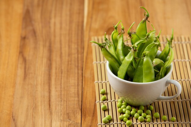 Petits pois placés dans une tasse sur une table en bois