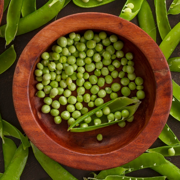 Photo gratuite petits pois à plat dans un bol en bois avec des gousses