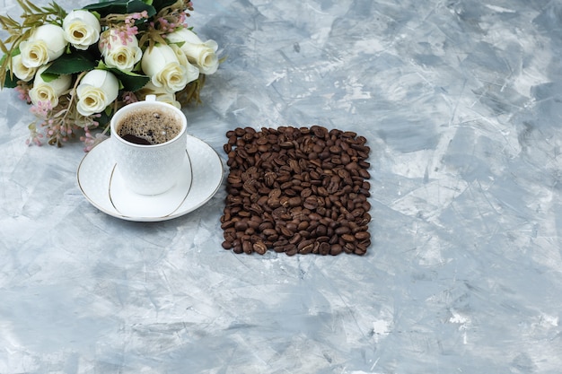 Un peu de café avec des grains de café, des fleurs dans une tasse sur fond de marbre bleu, vue grand angle.