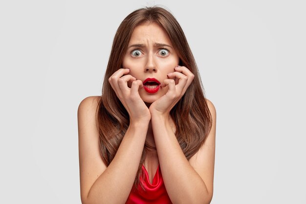 Peur de jeune femme brune posant contre le mur blanc