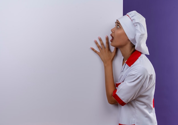 Photo gratuite peur jeune femme cuisinier portant l'uniforme de chef tenant un mur blanc sur fond isolé avec copie espace