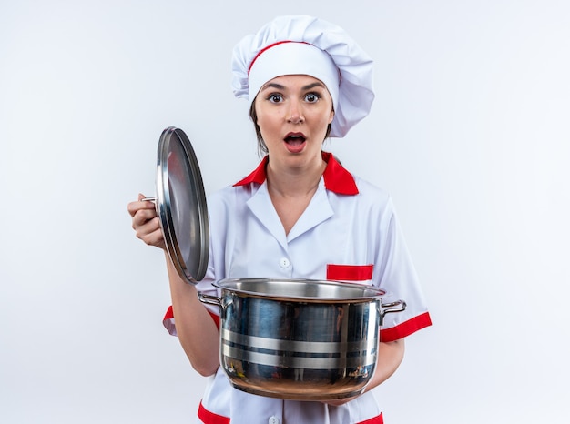 Peur jeune femme cuisinier portant l'uniforme du chef tenant une casserole avec couvercle isolé sur fond blanc