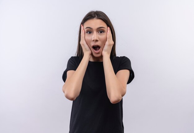 Peur de jeune fille caucasienne portant un t-shirt noir a mis ses mains sur la joue sur fond blanc isolé