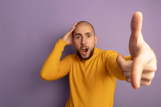 Photo gratuite peur à la recherche tout droit jeune beau mec pointe à la caméra en mettant la main sur la tête isolé sur violet