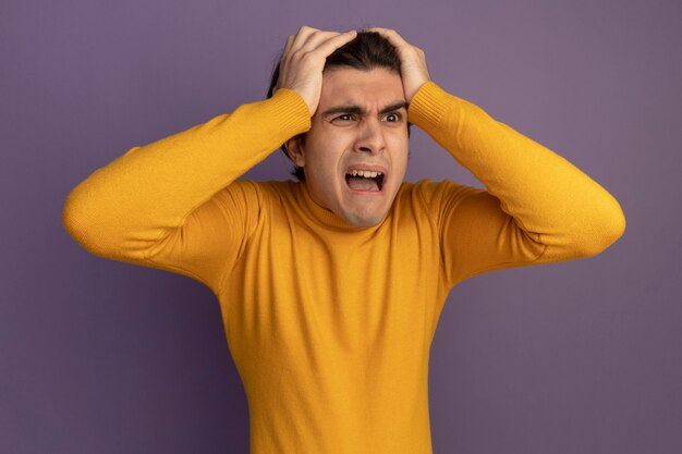 Peur en regardant côté jeune beau mec portant un pull à col roulé jaune attrapé la tête isolée sur le mur violet