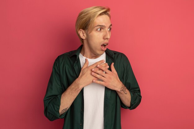 Peur regardant côté jeune mec blond portant un t-shirt vert mettant les mains sur le coeur