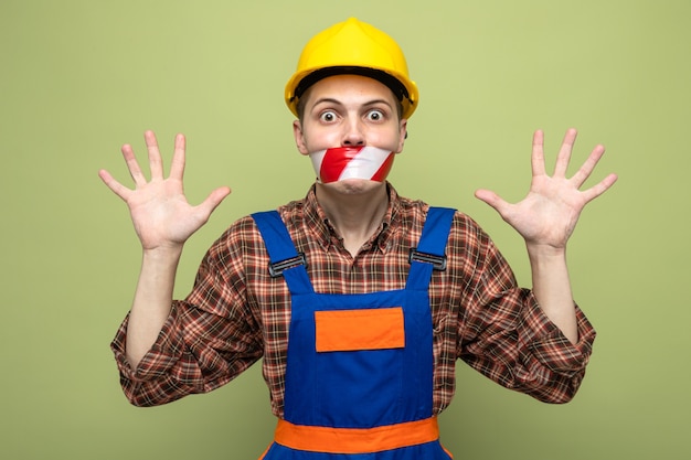 Peur de répandre les mains jeune constructeur masculin portant une bouche scellée uniforme avec du ruban adhésif