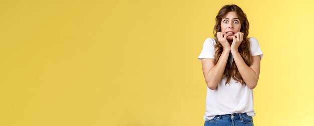 Peur timide peu sûr fille européenne coupe de cheveux bouclés tenir la main face aux doigts mordants regarder fr