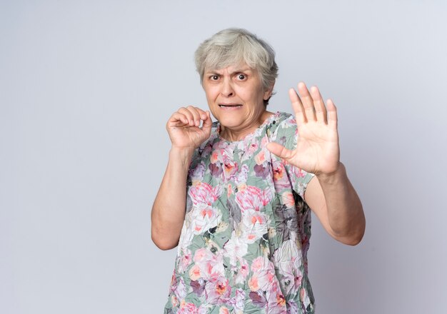 Peur vieille femme se tient avec les mains surélevées isolé sur mur blanc