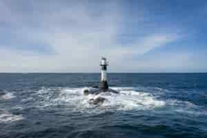 Photo gratuite phare au milieu de la mer sous le ciel nuageux