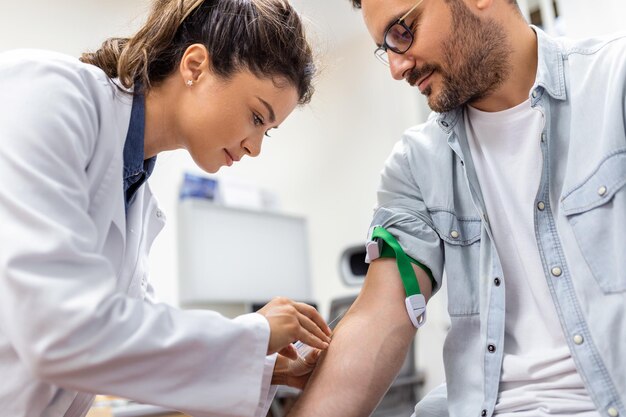 Phlébotomiste de l'hôpital amical recueillant un échantillon de sang d'un patient en laboratoire Préparation pour un test sanguin par une femme médecin uniforme médical sur la table dans une pièce blanche et lumineuse