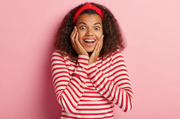 Photo d'une adolescente excitée aux cheveux bouclés posant en pull rouge rayé