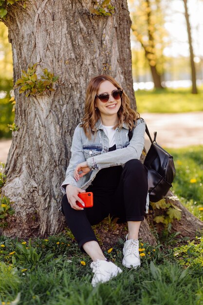 Photo d'une adolescente positive et joyeuse passe du temps dans le parc et utilise un téléphone portable.