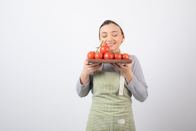 Photo d'une adorable jeune femme sent les tomates rouges sur un mur blanc