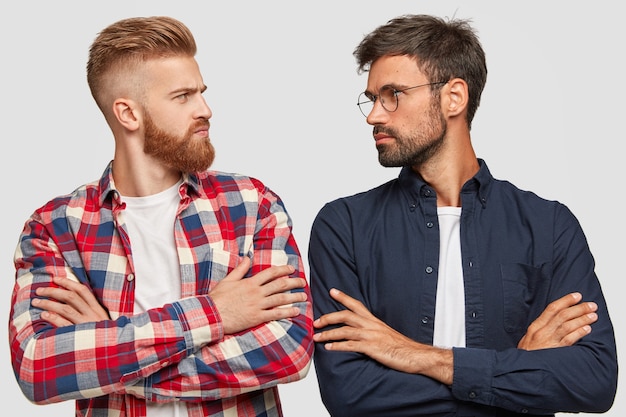 Photo gratuite photo d'adversaires masculins sérieux se tenant les mains croisées, se regardent, se font concurrence, se tiennent épaule contre épaule