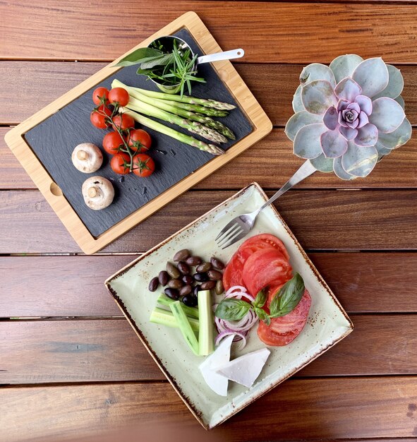 Photo aérienne de salade de haricots et de fromage sur une assiette près d'un plateau en bois avec légumes près de rose