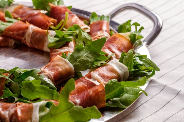 Photo de bacon roule avec roquette sur mur blanc.