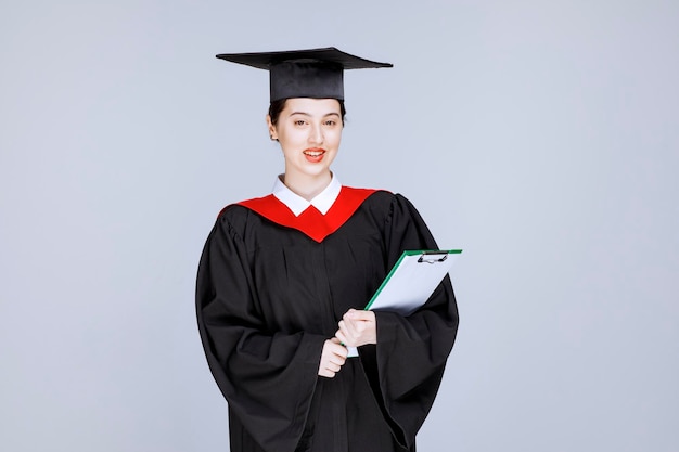 Photo de belle étudiante diplômée avec presse-papiers posant. photo de haute qualité