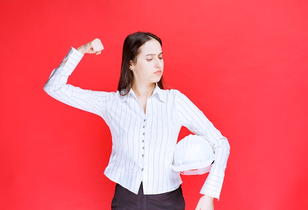 Photo d'une belle femme d'affaires tenant un chapeau de sécurité et montrant du muscle.