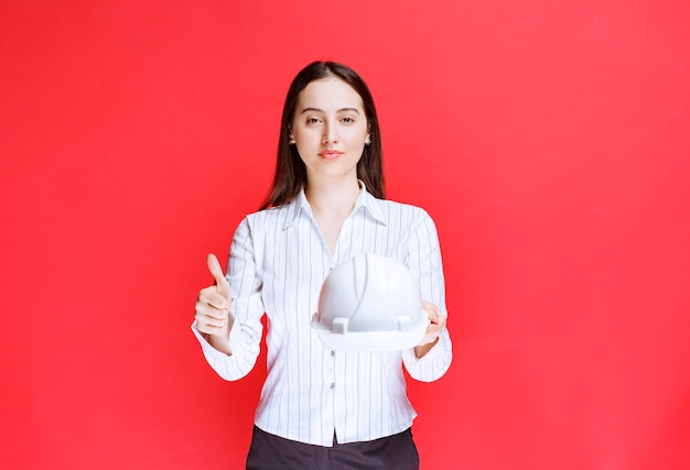 Photo d'une belle femme d'affaires tenant un chapeau de sécurité et montrant un pouce vers le haut.