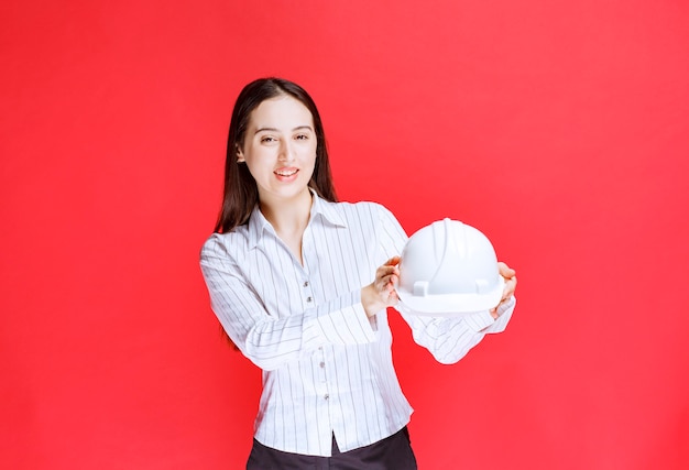Photo d'une belle femme d'affaires tenant un chapeau de sécurité sur un mur rouge.
