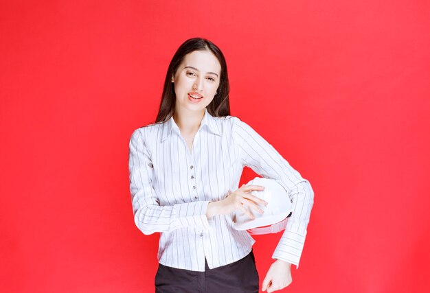 Photo d'une belle femme d'affaires tenant un chapeau de sécurité sur un mur rouge.